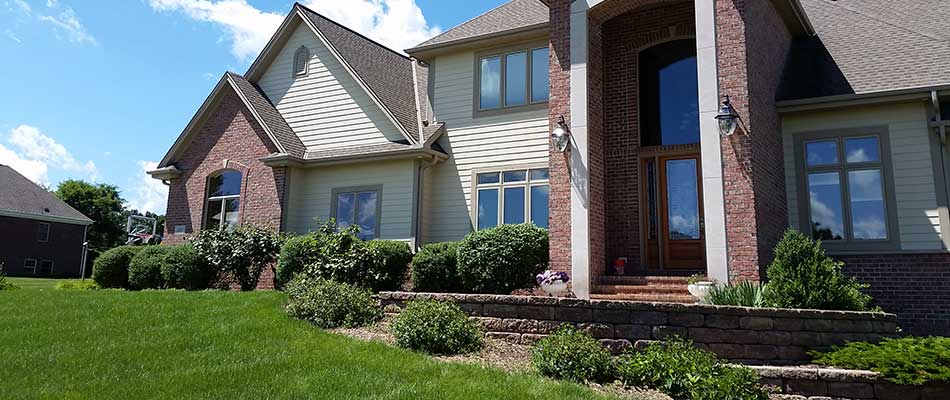 Suburban house with brick and siding façade, large windows, arched entryway, landscaped lawn, under a clear blue sky. No people visible.