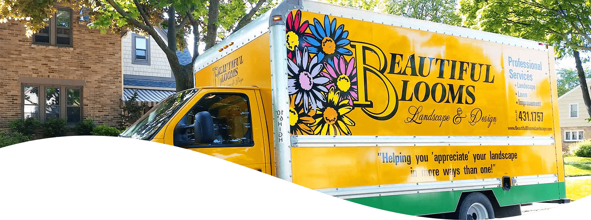 A colorful landscaping company truck is parked on a residential street, with vibrant flower graphics and advertising text on its side.